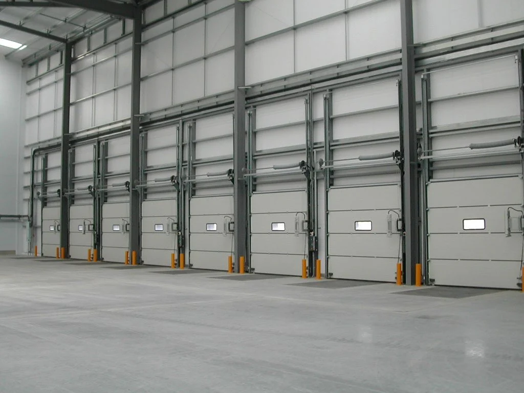 Row of white sectional overhead doors with windows along a warehouse loading bay