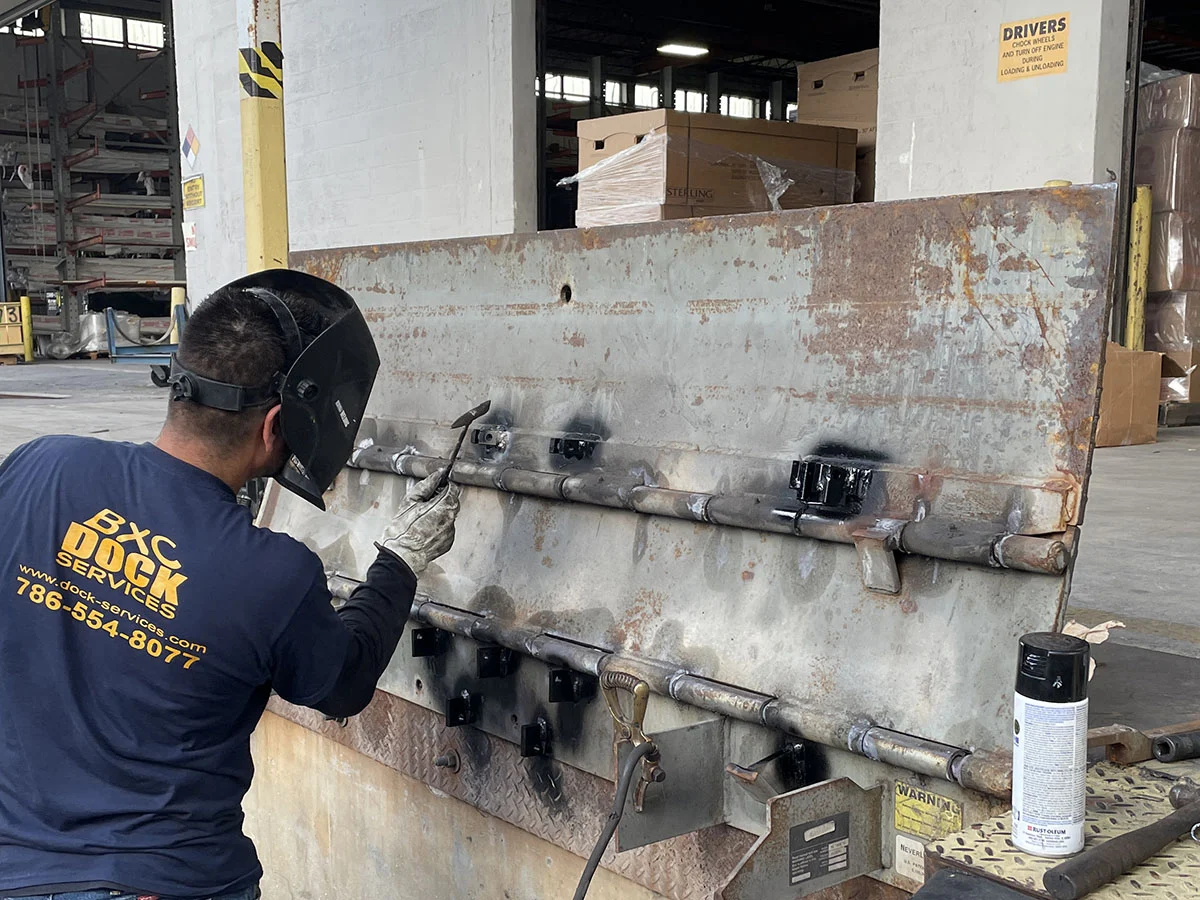 BXC technician welding an edge of dock leveler hinge repair