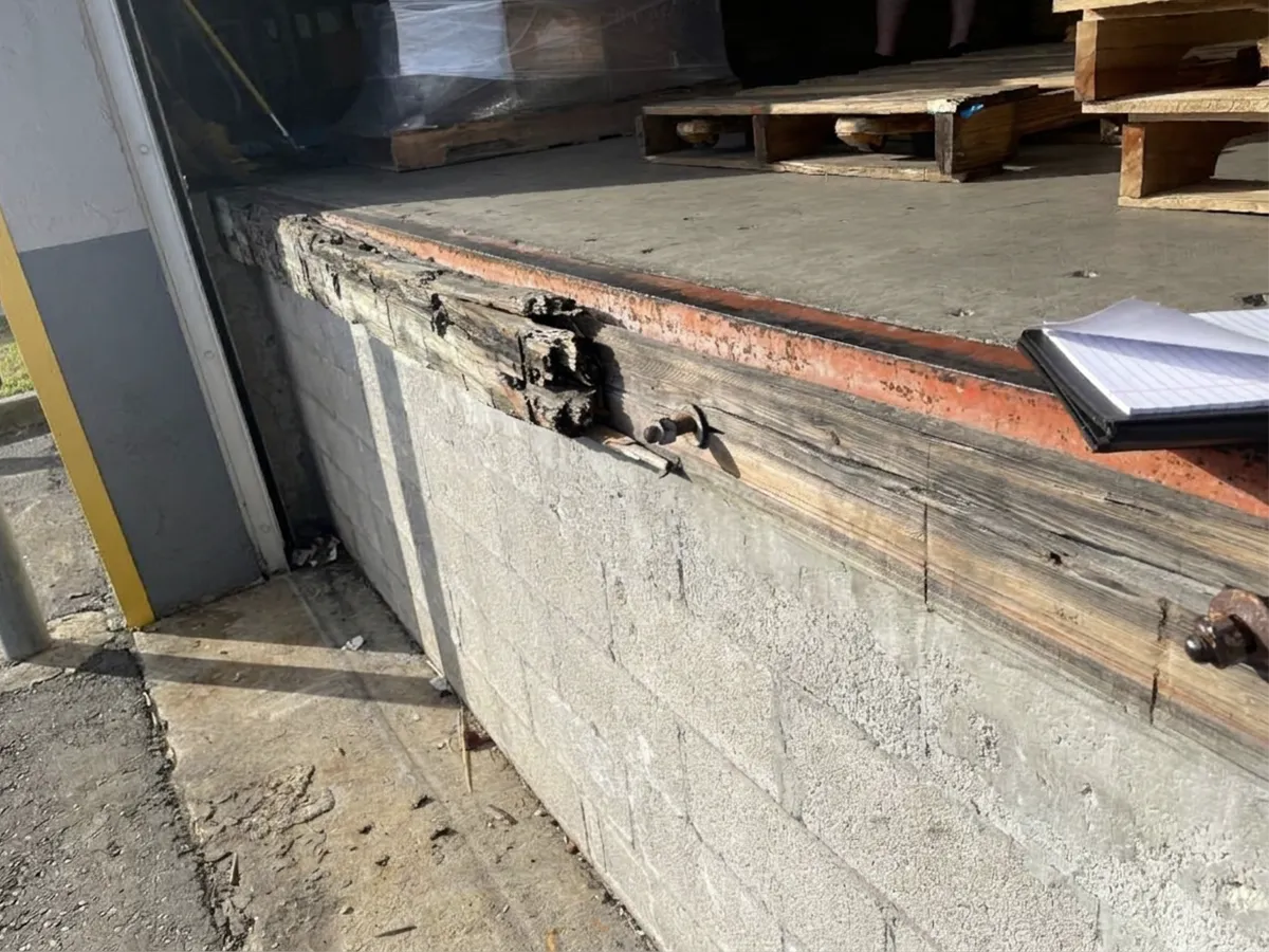 Loading dock edge with rotted wood and the overhead door track flush to the dock face, before a recessed edge of dock leveler